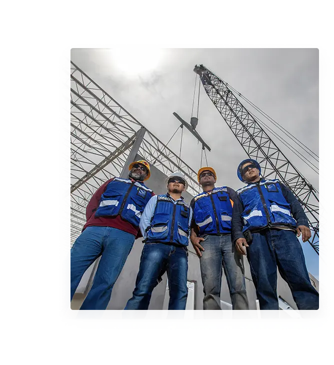 About DAVISA. A group of construction workers posing in front of a crane in an industrial building construction site while wearing blue safety gear